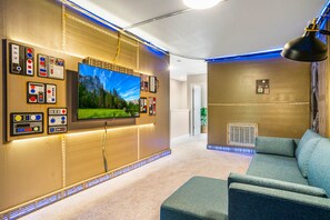 Ein modernes Wohnzimmer mit großem Flachbildfernseher an der Wand, einer gemütlichen Couch und einer Deckenleuchte.