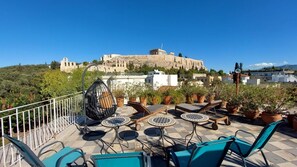 Une terrasse sur le toit, aménagée avec des espaces de détente en plein air, des plantes en pot et offrant une vue sur un château ancien.
