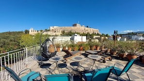 Eine Dachterrasse mit Sitzgelegenheiten im Freien, Topfpflanzen und Blick auf eine alte Burg.