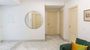 A hallway with a round mirror, beige doors, and a green sofa with a yellow pillow.