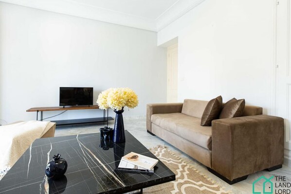 A modern living room with a black coffee table, a beige sofa, a flat-screen TV, and a vase with flowers.