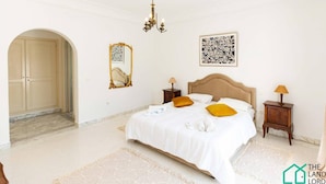 A hotel room with a large bed, two bedside tables, a chandelier, a mirror, and artwork on the walls.