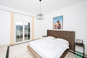 Une chambre d’hôtel avec un lit, une table de chevet, un magazine accroché au mur et une vue par les portes coulissantes.