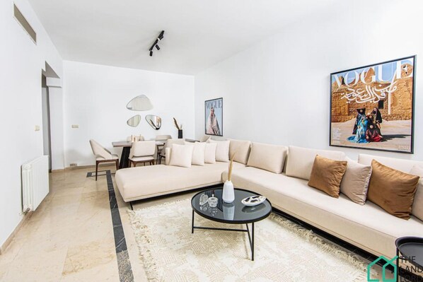 Un salon moderne avec un canapé beige, une table basse ronde et un coin repas comprenant une table et des chaises.