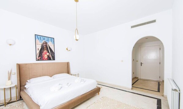 A minimalist bedroom with a large bed, a Vogue magazine on the wall, and a white door. - Le Parfait II Bord de mer Central et Luxueux (La Marsa)