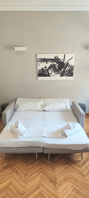 A neatly made bed with white linens and towels, a gray upholstered headboard, and a herringbone wooden floor.