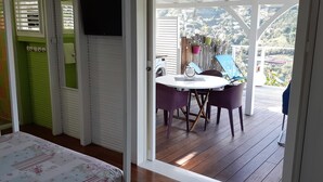 A room with a bed, a table with chairs, and a view of a balcony with plants and a chair. - A LOU, A haven of peace with its private jacuzzi for nature lovers ! (Le Diamant)