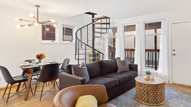A modern living room with a brown leather armchair, a dark brown sofa, a round wooden coffee table, and a spiral staircase. - Comfort, Style, Short Walk To Town Park & Gondola 1 Bedroom Condo by RedAwning (Telluride)