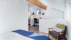 A bedroom with a bed, a chair, a desk, and a kitchenette in the background. - Comfort, Style, Short Walk To Town Park & Gondola 1 Bedroom Condo by RedAwning (Telluride)