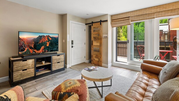 A living room with a TV, sofa, coffee table, and a sliding door leading to a balcony. - Ski In/out In Town! Ski Area Views, Fireplace, Hot Tub 2 Bedroom Condo by RedAwning (Telluride)
