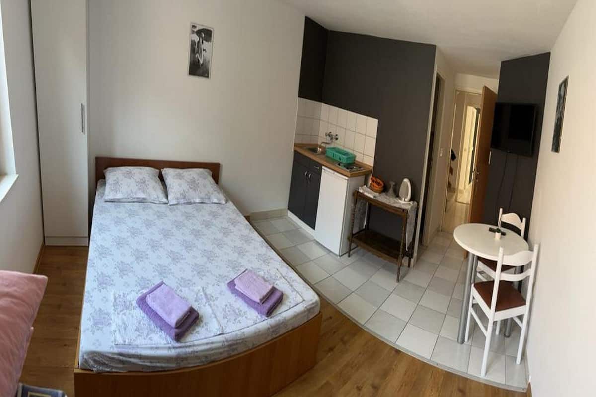A bedroom with a bed, a small desk, a chair, and a TV.