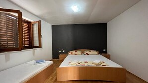 A bedroom with a bed, a bedside table, a nightstand, a window with blinds, and a ceiling light. - Apartments Leut (Omis)