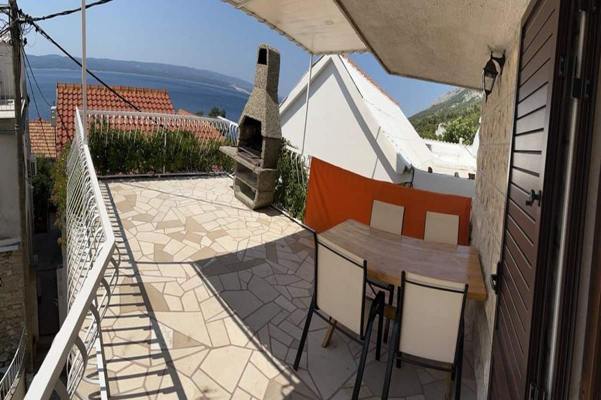 A patio with a stone floor, a barbecue grill, and a table and chairs.