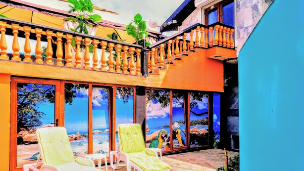 Een balkon met twee ligbedden, uitzicht op zee door grote ramen en een houten balustrade.