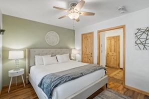 A bedroom with a bed, a ceiling fan, a wall-mounted light, a bedside table, and two wooden doors. - Modern Comfort River/mtn Views + Hot Tub 1 Bedroom Condo by RedAwning (Telluride)