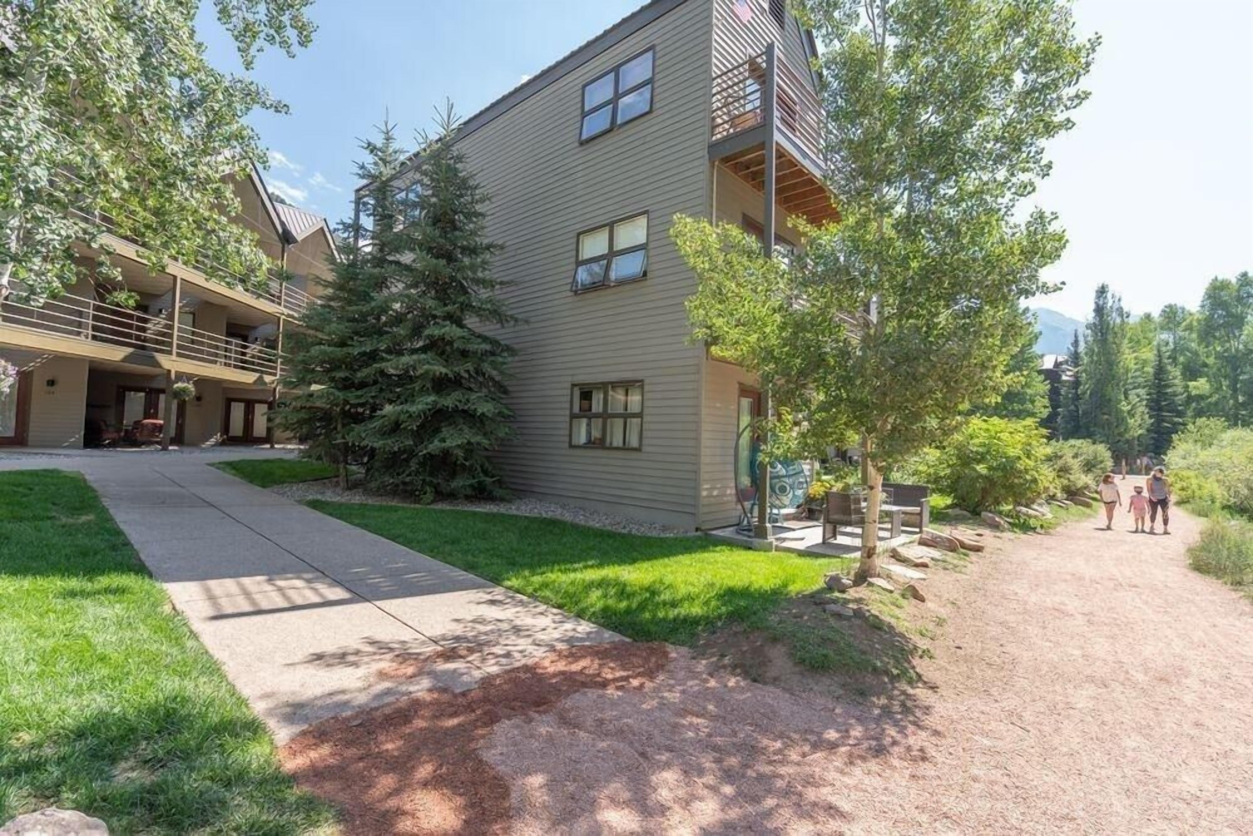 A multi-story building with a covered outdoor area, a gravel path, and a well-maintained lawn.
