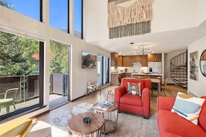 A spacious living area with a red sofa, a coffee table, and a view of the outdoors through large windows. - Hidden Gem, 4 Min To Lift 7 Garage, Hot Tub, Lux Kitchen, Big + Bright 4 Bedroom Condo by RedAwning (Telluride)