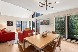 A modern living room with a wooden dining table, red sofas, and a large window with a mountain view. - Hidden Gem, 4 Min To Lift 7 Garage, Hot Tub, Lux Kitchen, Big + Bright 4 Bedroom Condo by RedAwning (Telluride)