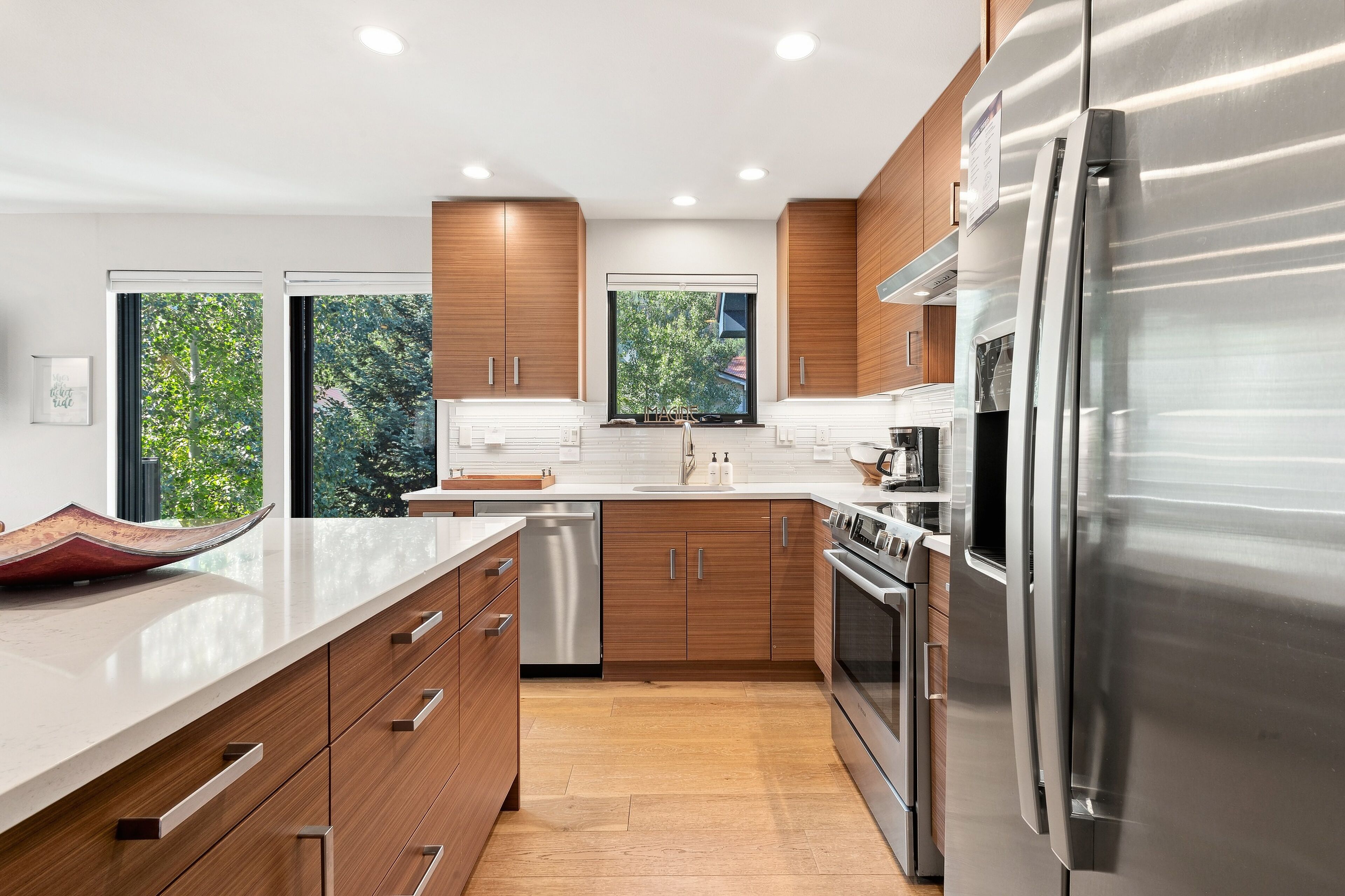 Une cuisine moderne avec des meubles en bois, des appareils en acier inoxydable et une grande fenêtre offrant une vue sur la verdure.