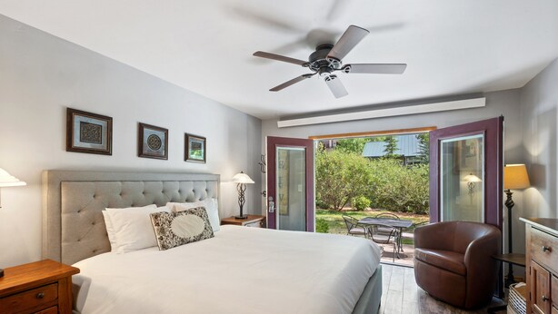 A bedroom with a large bed, a ceiling fan, a view through an open door, and a small patio area. - Ground Floor On River Trail, Walk To Ski 1 Bedroom Condo by RedAwning (Telluride)