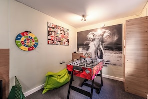 Een kamer met een tafelvoetbaltafel, dartbord en een muur met een foto en een agenda.
