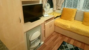 A compact room with a bed, a TV, a fan, and a window with curtains. - Remarkable Caravan in Abergele Towyn (Abergele)