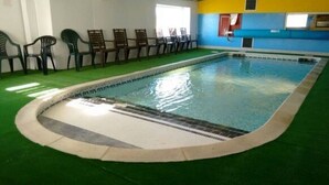 An indoor swimming pool with a green artificial turf floor, surrounded by chairs and a blue wall with windows. - Remarkable Caravan in Abergele Towyn (Abergele)