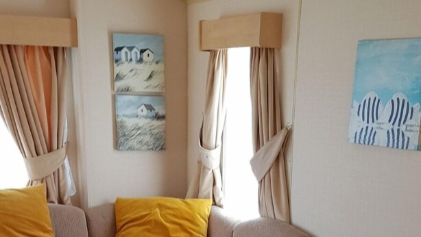 A cozy room with a sofa, a dining table, and artwork on the walls. - Remarkable Caravan in Abergele Towyn (Abergele)