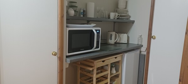 A compact kitchen with a microwave, kettle, and stacked dishes on shelves. - Relax With Amazing Views! 1-bed Studio in Tegryn (Llanfyrnach)