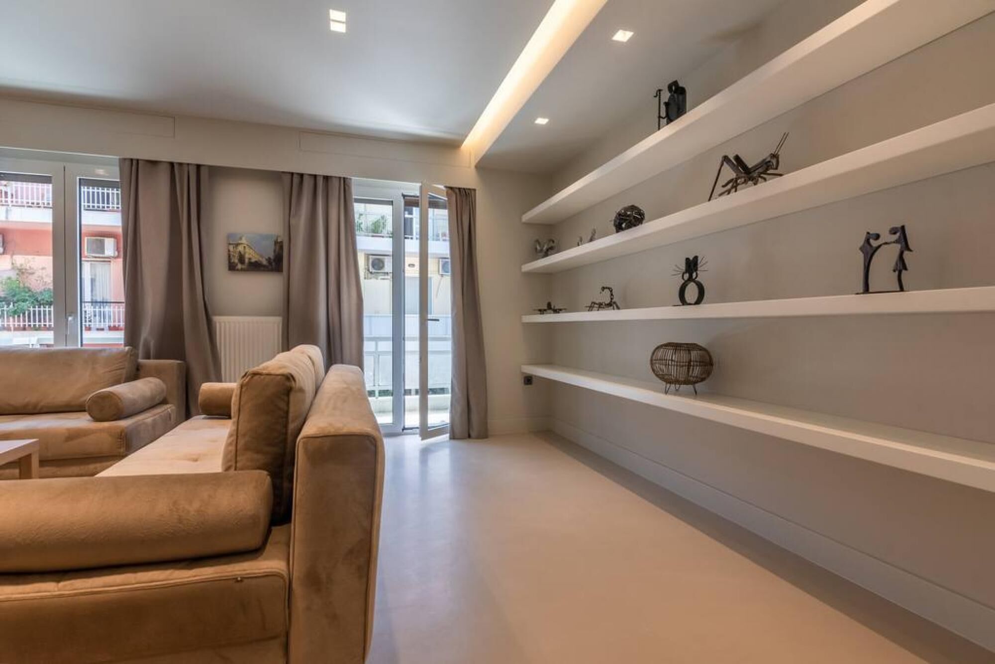 A modern living room with a sofa set, a glass door leading outside, and a wall with decorative shelves.