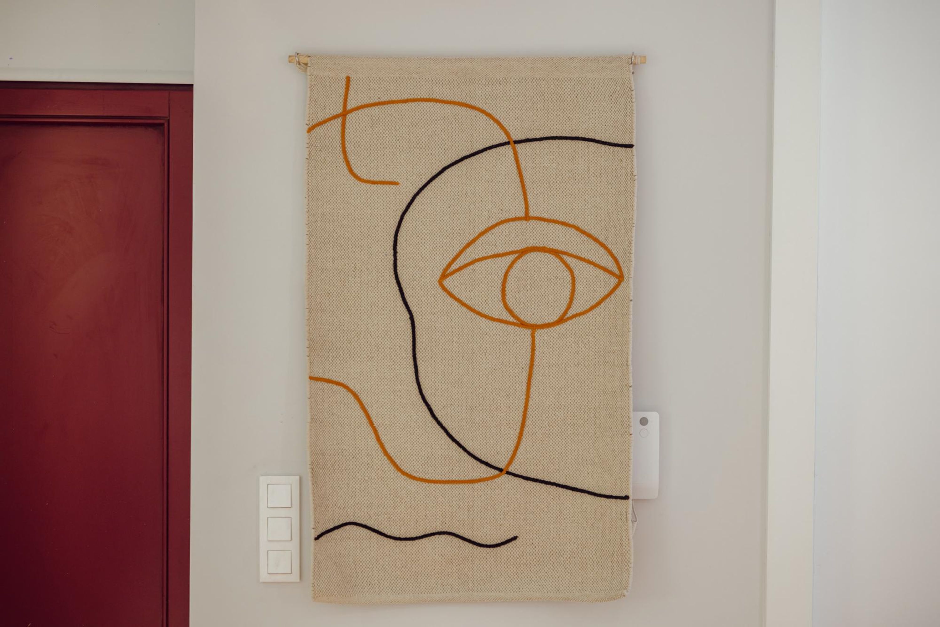 Parede com uma obra de arte abstrata pendurada e uma porta vermelha.