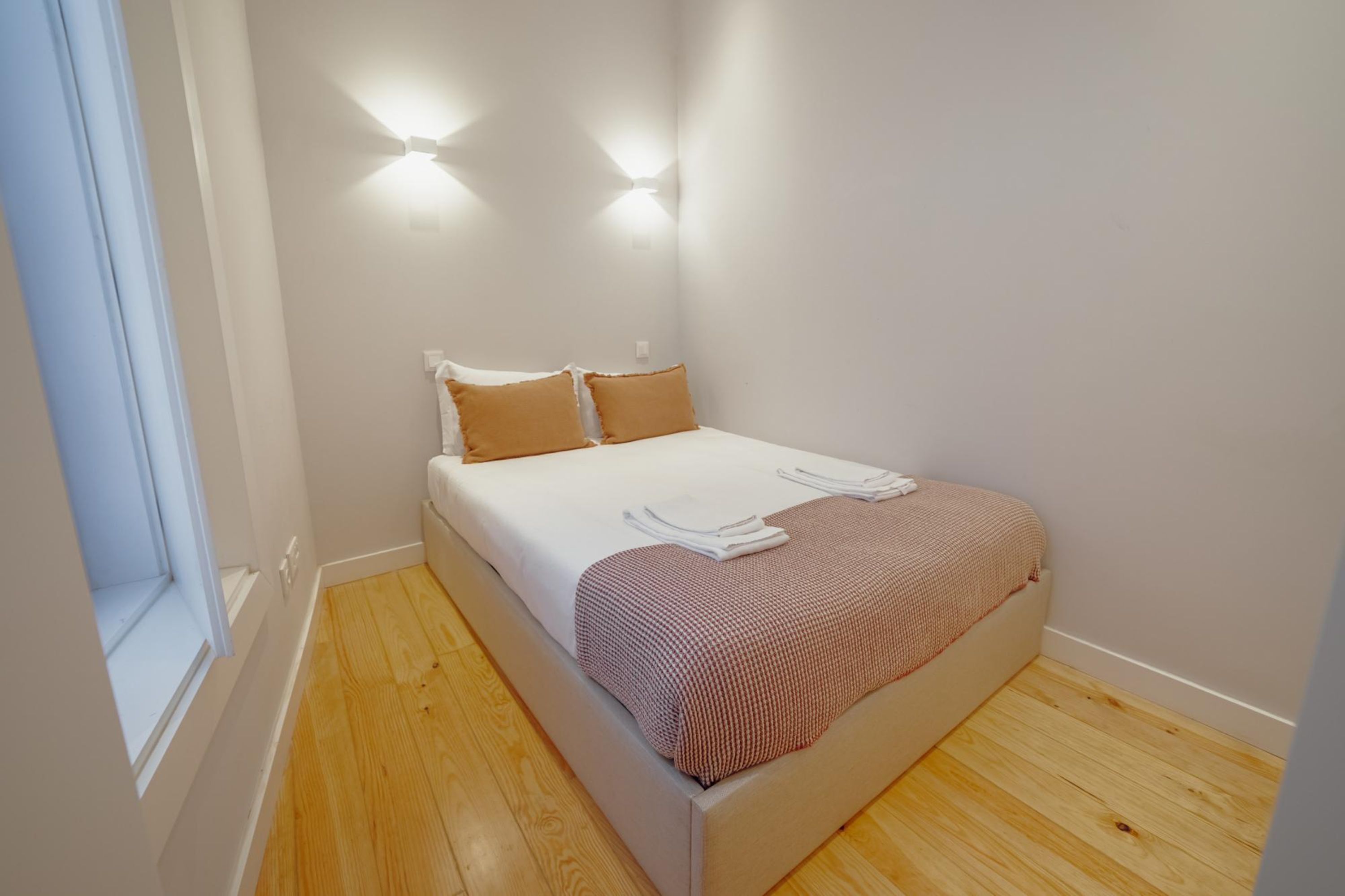 Un letto piccolo e ben rifatto con una coperta bianca e marrone a quadri, due cuscini e una finestra sul lato sinistro.