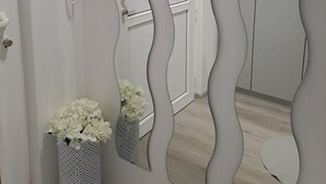Un baño con un espejo de diseño ondulado, un teléfono y un jarrón con flores blancas.