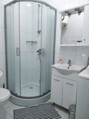 A modern bathroom with a glass-enclosed shower, a white sink, and a toilet. - Apartment Dream (Osijek)