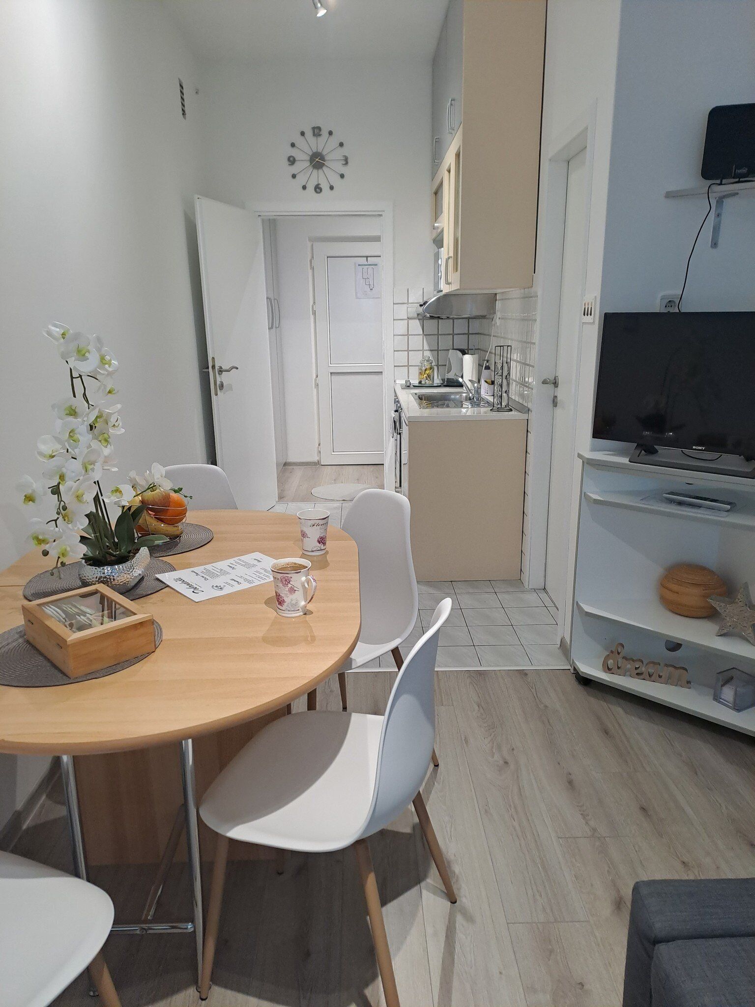 Una cocina moderna con armarios blancos, horno empotrado y microondas. Cuenta con un comedor con mesa de madera y sillas blancas.