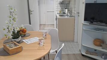Una cocina moderna con armarios blancos, horno empotrado y microondas. Cuenta con un comedor con mesa de madera y sillas blancas.