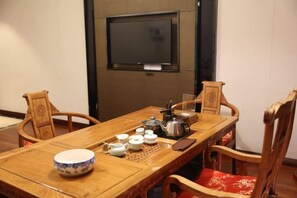 A wooden dining table with chairs, a television mounted on the wall, and various tea utensils. - Tibet Ali Hotel (Gar County)