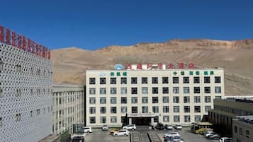 A multi-story building with a parking lot in front, surrounded by a mountainous landscape.