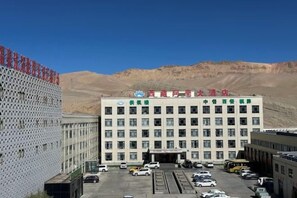 A multi-story building with a parking lot in front, surrounded by a mountainous landscape. - Tibet Ali Hotel (Gar County)