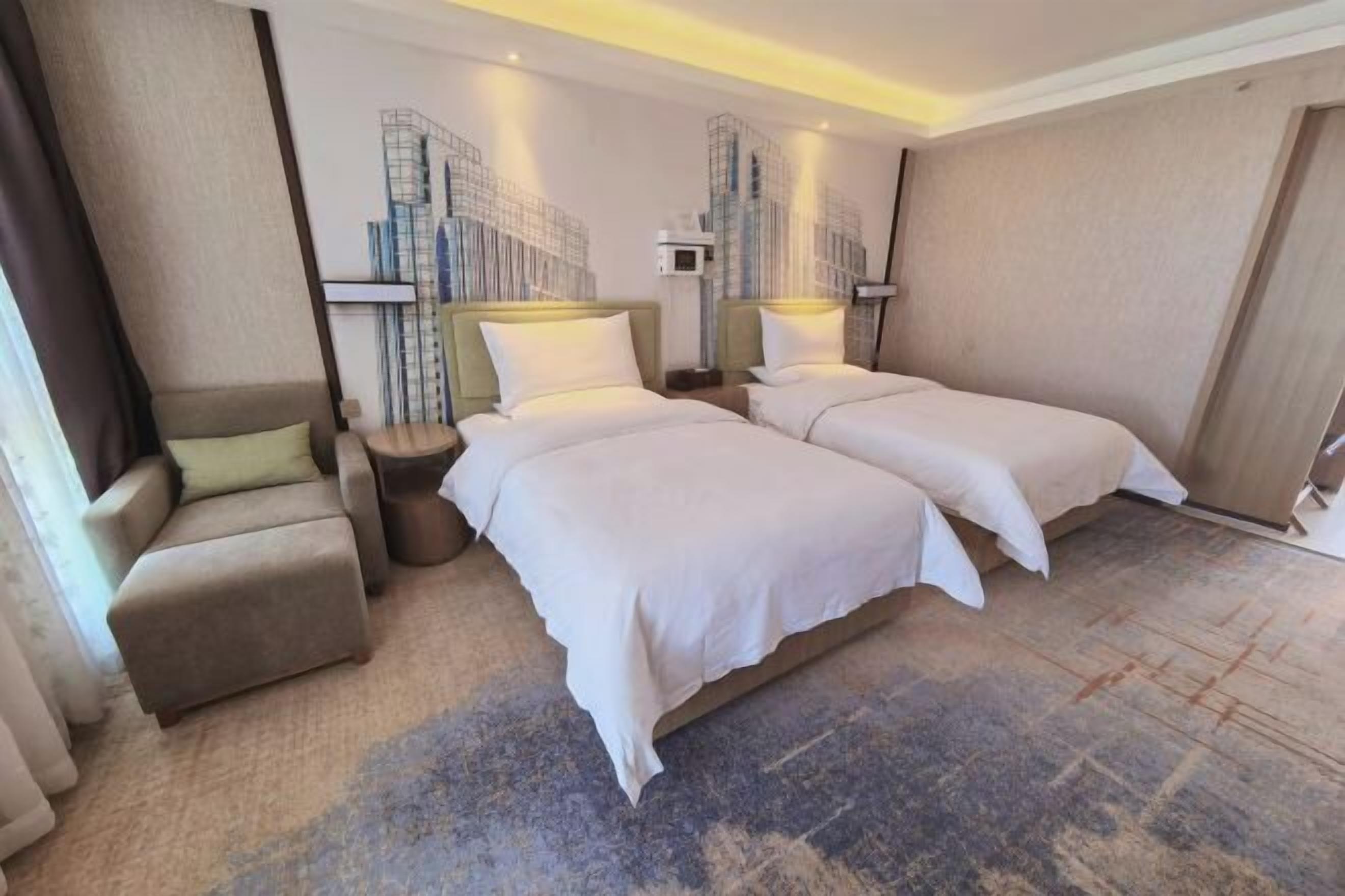 A hotel room with two beds, a sofa, a small table, and a wall-mounted TV.