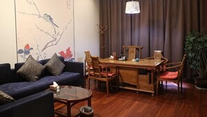A living room with a sofa, coffee table, dining table, chairs, a hanging light fixture, and a wall with artwork.
