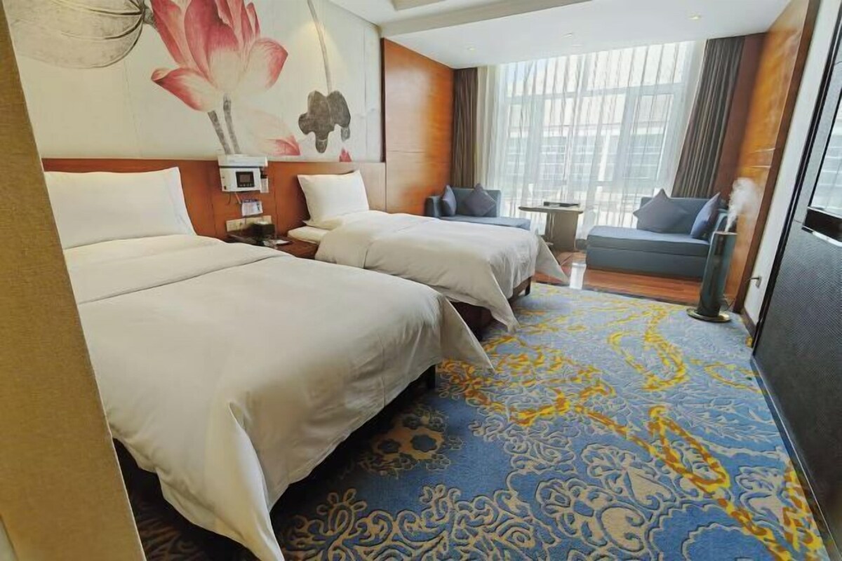 A hotel room with two beds, a sofa, a small table, and a large window.