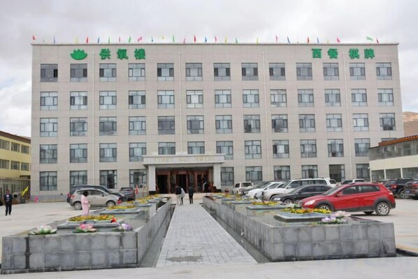 A multi-story building with a central entrance, surrounded by a parking area with several cars. - Tibet Ali Hotel (Gar County)