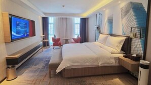A hotel room with a large bed, a TV mounted on the wall, a small table, two chairs, and a window with curtains. - Tibet Ali Hotel (Gar County)