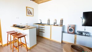 Eine kleine Küche mit einer Holzinsel, Barhocker, einem Flachbildfernseher und einem Lautsprecher.