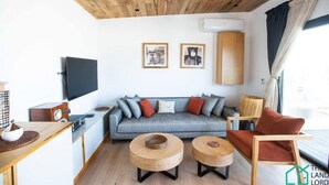Ein modernes Wohnzimmer mit einem grauen Sofa, zwei runden Holztischen, einem Flachbildfernseher und gerahmten Kunstwerken an der Wand.