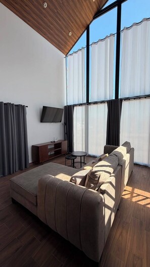 Ein modernes Wohnzimmer mit einer großen Eckcouch, einem flachbildfernseher an der Wand und einer Holzbalkendecke.