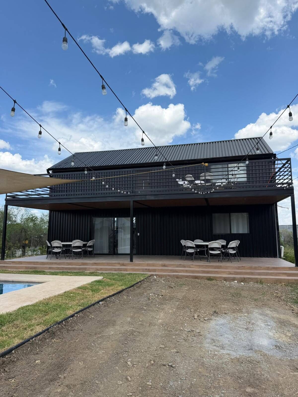 Un edificio moderno de dos pisos con techo plano, zona de estar al aire libre y piscina.