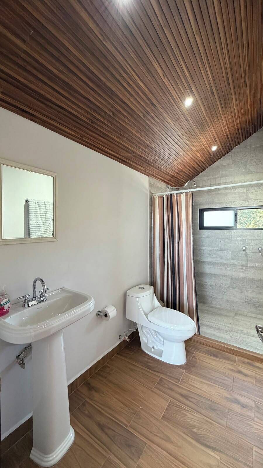 A bathroom with a wooden ceiling, a white sink, a toilet, and a shower curtain.
