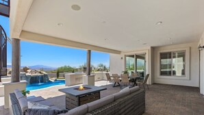 A covered patio with a fire pit, outdoor seating, and a view of a pool and mountains.